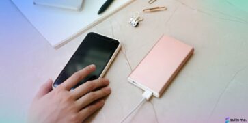 Mobile phone on a desk being charged with a woman's hand reaching for the phone to log into their mobile banking app
